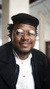 Confident man in glasses with a stylish hat smiling indoors.